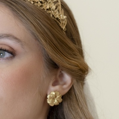 Brinco dourado em forma de flor e coroa dourada decorada com flores num fundo bege.