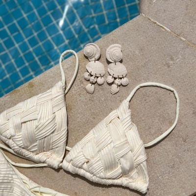 Biquíni branco trançado com brincos de conchas ao lado de piscina azulejada