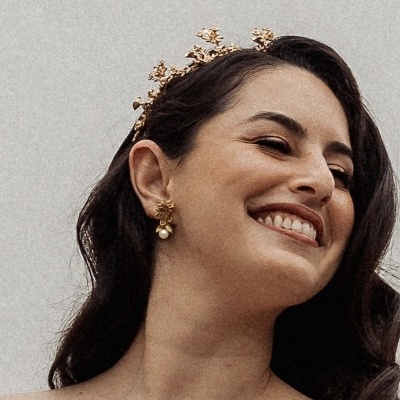 Mulher sorridente com tiara dourada floral e brincos dourados com pérolas
