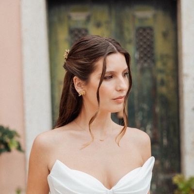 Mulher com corset branco de tecido acetinado e cabelo castanho com acessório dourado