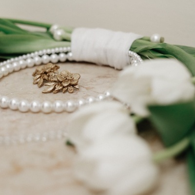 Flores brancas com folhas verdes, colar de pérolas e brincos dourados sacados juntos