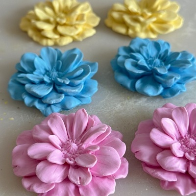 Seis flores decorativas coloridas azul, amarelo e rosa sobre superfície cinzenta.