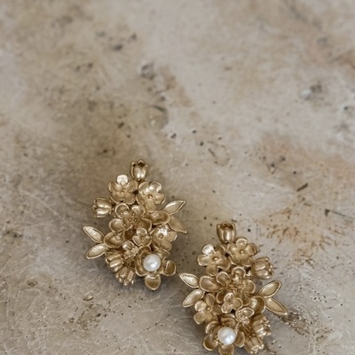 Brincos dourados com flores e pérolas em superfície bege irregular