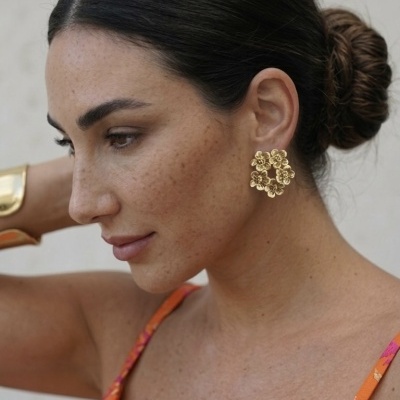 Mulher com brincos dourados de flores e vestido laranja com padrão floral.