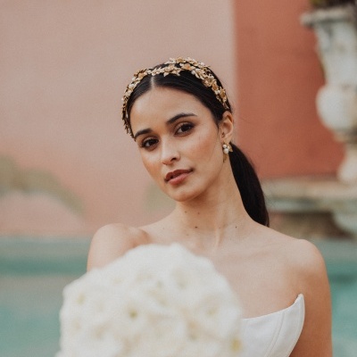Mulher com vestido e tiara dourada segurando bouquet de flores brancas