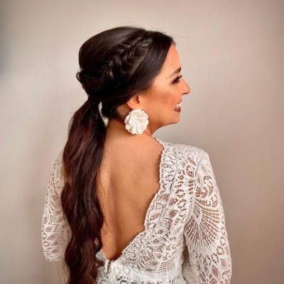 Mulher com vestido branco de renda e brinco grande branco em ambiente neutro