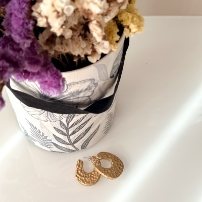 Brincos dourados martelados junto a vaso decorativo com flores secas