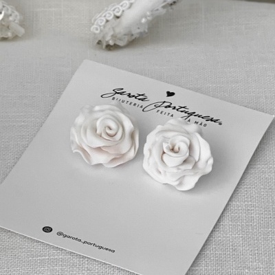 Brincos em forma de rosas brancas e rosa claro em cartão com texto e suporte branco bordado ao fundo