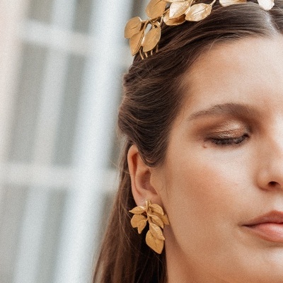 Tiara e brincos dourados de folhas em mulher, fundo desfocado branco