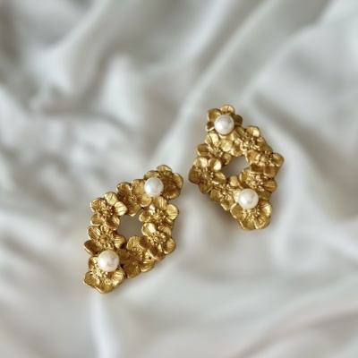 Brincos dourados com flores e pérolas sobre tecido branco