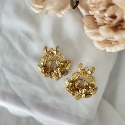 brincos dourados com flores sobre tecido branco e flores artificiais