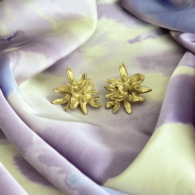 Brincos dourados com design floral sobre tecido lilás e verde