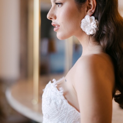 Mulher com vestido branco detalhado e brincos grandes florais brancos em ambiente interior