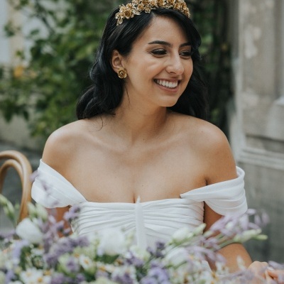 Mulher com vestido branco e tiara dourada sentada à mesa com flores