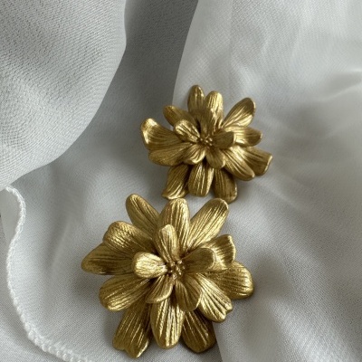 Brincos dourados em forma de flores sobre tecido branco