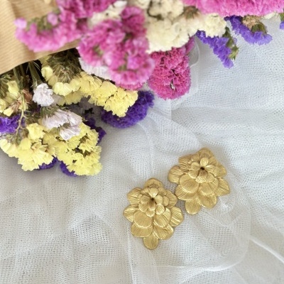 Brincos dourados em forma de flor sobre tecido branco com flores secas coloridas