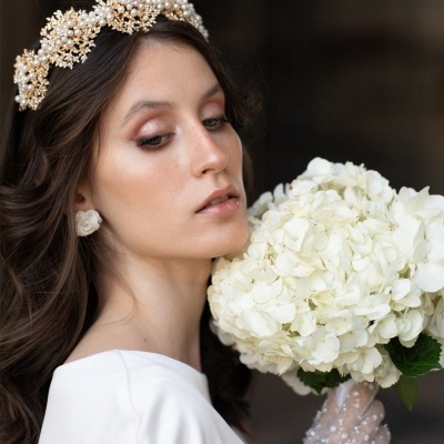 Mulher com vestido branco, tiara perolada, luvas transparentes com pontos e buquê de hortênsias brancas
