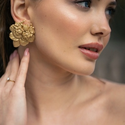 Mulher com brinco dourado grande de flores e anel dourado simples