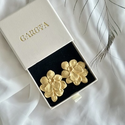 Brincos dourados florais numa caixa branca com o texto GARCEA
