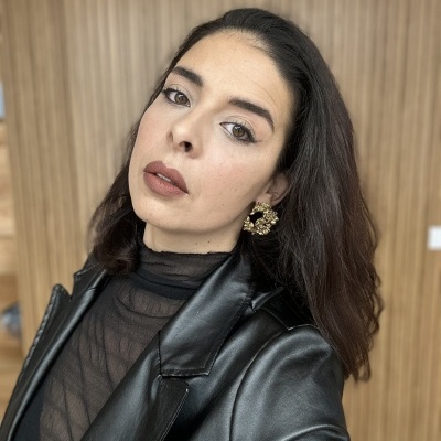 Mulher com casaco preto de material sintético brilhante e brincos dourados grandes com textura floral