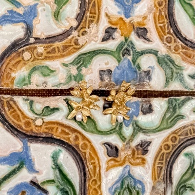 Brincos dourados com flores e pérolas sobre azulejos coloridos