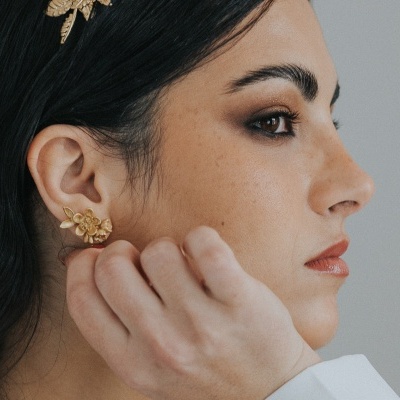 Brincos dourados florais em mulher com maquilhagem neutra e acessórios dourados no cabelo