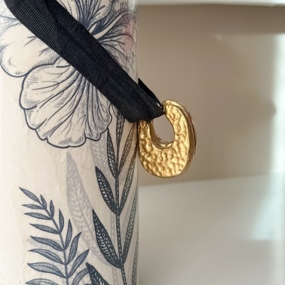 Saco cilíndrico com padrão floral preto e laço preto com pendente dourado.