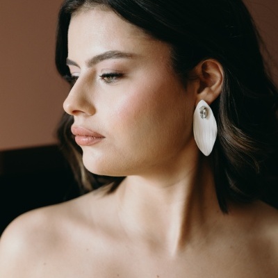 Brincos grandes brancos em forma de folha com detalhe prateado numa mulher