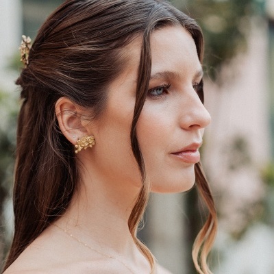 Mulher com brincos dourados e presilha floral no cabelo castanho