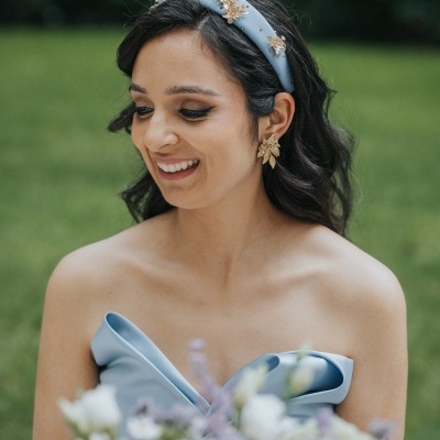 Mulher com vestido azul claro e acessórios dourados em ambiente exterior