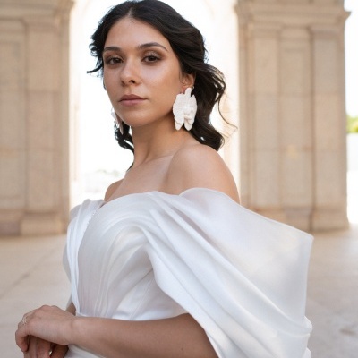 Mulher com vestido branco elegante e brincos grandes em fundo arquitetónico