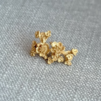 Broche dourado em forma de flores sobre tecido cinza.