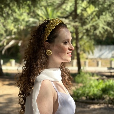 Mulher de perfil com faixa de cabelo dourada e vestido branco ao ar livre