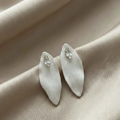 Brincos em formato de pétala branca com pedra transparente sobre tecido bege