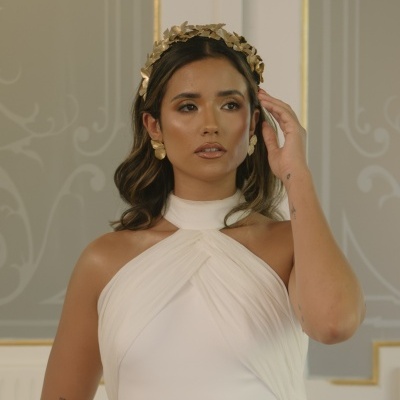 Mulher com vestido branco e acessórios dourados num interior elegante
