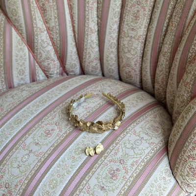 Colar e brincos dourados com flores sobre poltrona estofada listrada e floral