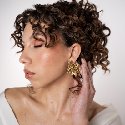 Brincos dourados florais usados por mulher com cabelo encaracolado e vestido branco