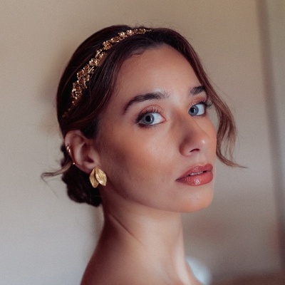 Mulher com tiara dourada e brincos grandes em fundo neutro