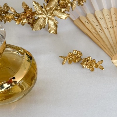 Tiaras e brincos dourados em forma de flores com leque e frasco de perfume