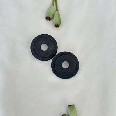 Dois discos pretos redondos com orifício central sobre tecido branco com cápsulas de papoila verdes ao redor