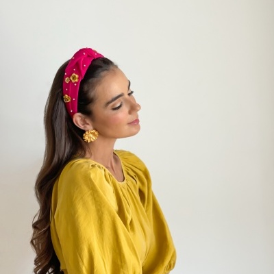 Mulher com vestido amarelo e faixa de cabelo rosa com detalhes dourados e brincos dourados