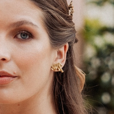 Mulher com brincos dourados de flores e cabelo preso com acessório dourado