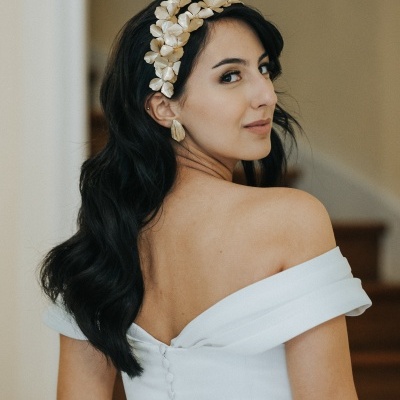 Mulher com fita de cabeça flores creme e vestido branco ombro a ombro num interior com escadas