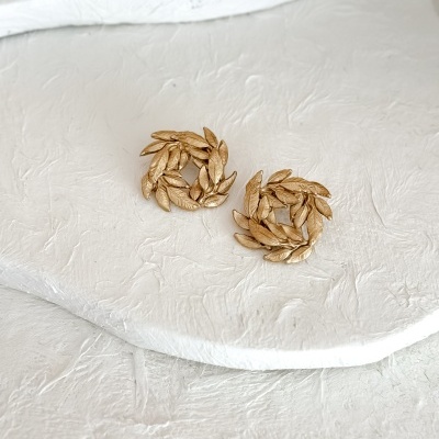 Brincos dourados redondos com folhas entrelaçadas sobre fundo branco texturizado