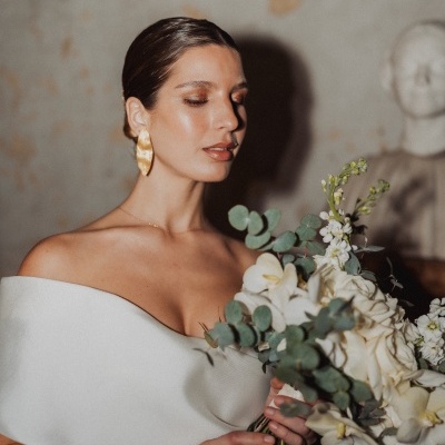 Mulher com vestido branco e brincos dourados a segurar bouquet de flores