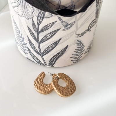 Brincos dourados martelados junto a caixa decorativa com padrão botânico