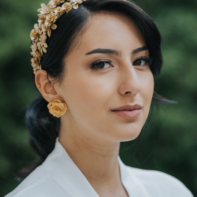 Mulher com diadema e brincos dourados, vestindo branco em fundo verde