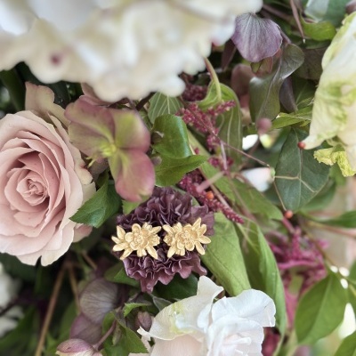 Brincos dourados em forma de flor sobre flores naturais coloridas