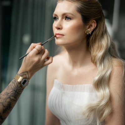 Mulher com vestido branco e coroa dourada a ser maquilhada