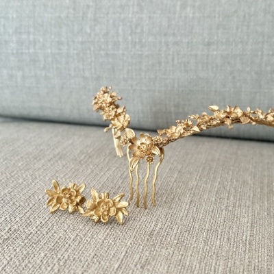 Conjunto de acessórios para cabelo dourados com design floral sobre tecido cinza claro